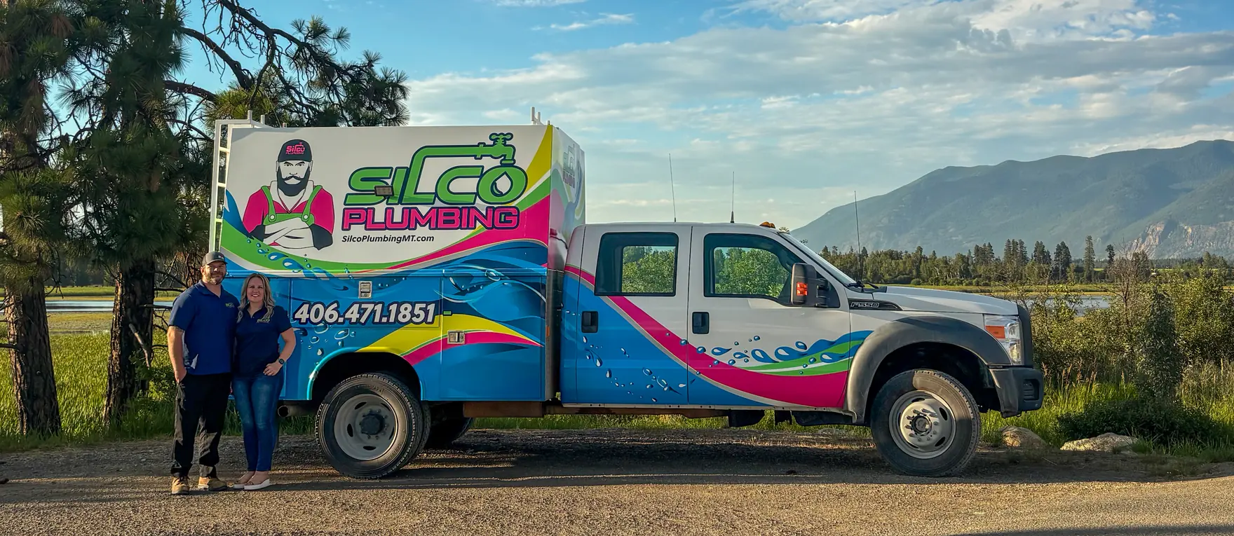 Silco Plumbing owners Andrew and Anali Silvius beside their wrapped service truck, Montana mountains behind them